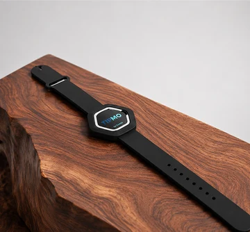 TIPMO Wristband — a black hexagonal NFC wearable on a silicone strap, resting on a polished wood block